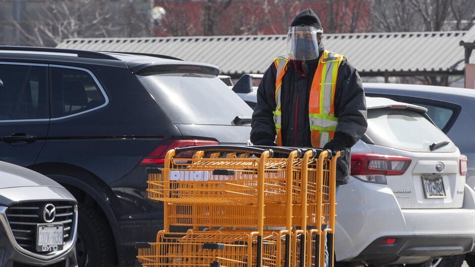 Un travailleur d'épicerie portant un masque et une visière pousse des paniers.