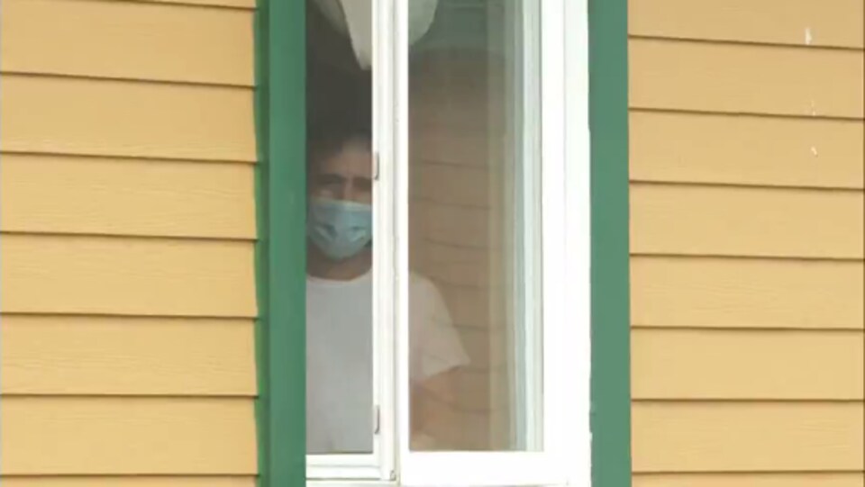 Un homme portant un masque regarde à travers une fenêtre.