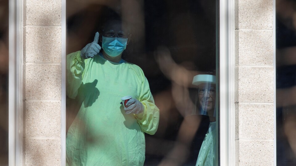 Des travailleurs de la santé sont derrière une fenêtre, dans un CHSLD.