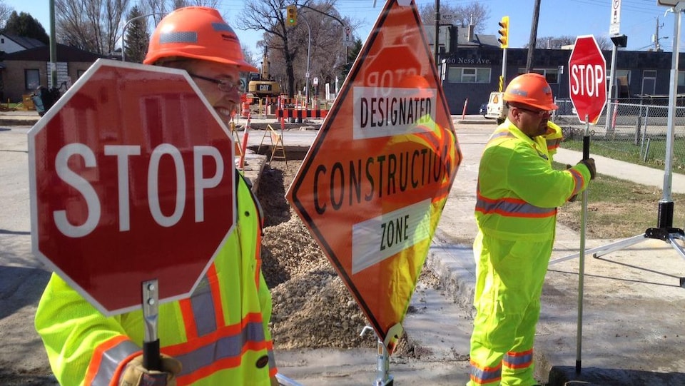 Des travailleurs de la construction tiennent des panneaux de signalisation sur un chantier.