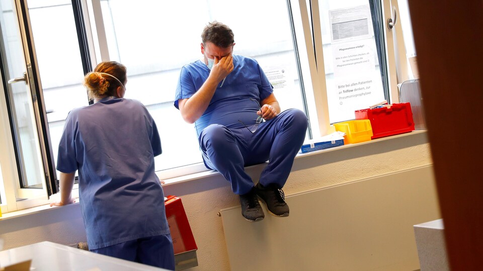 Un infirmier assis sur le rebord d'une fenêtre se masse les yeux avec la main. Une infirmière est près de lui.