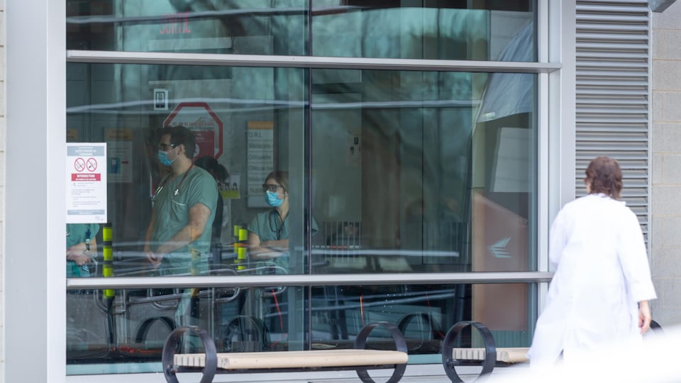 Des travailleurs de la santé, portant un masque, vus à travers une fenêtre de l'urgence du CHAUR de Trois-Rivières.