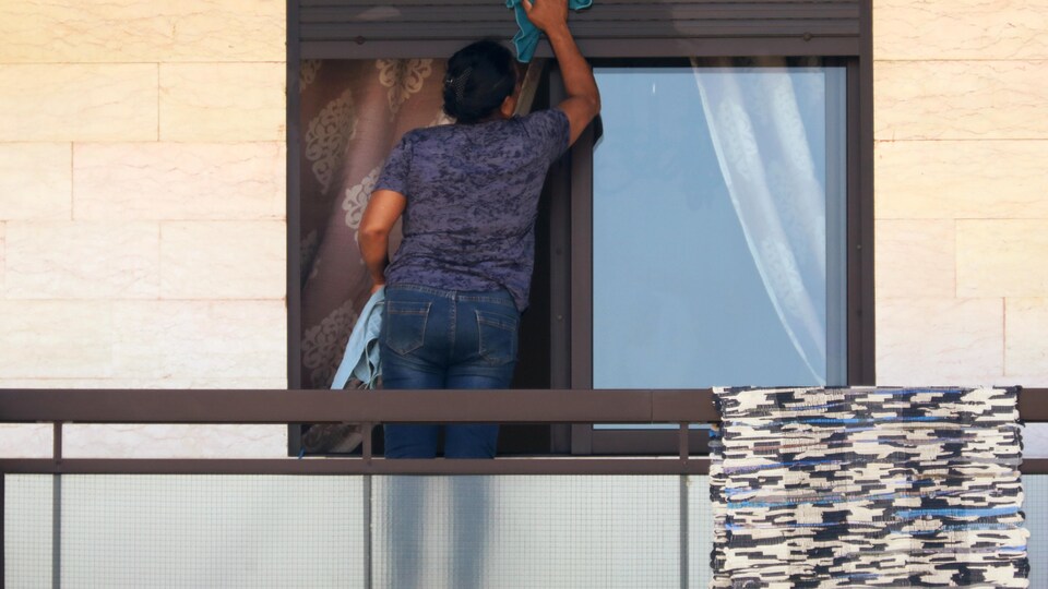 Une femme nettoie les vitres d'un appartement.