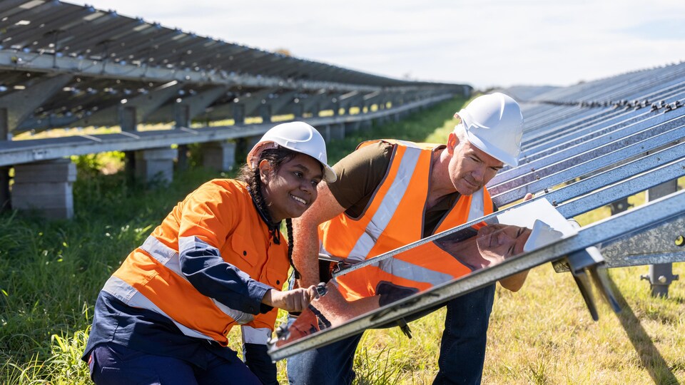 Un homme blanc et une femme aborigène travaillent sur un panneau solaire.