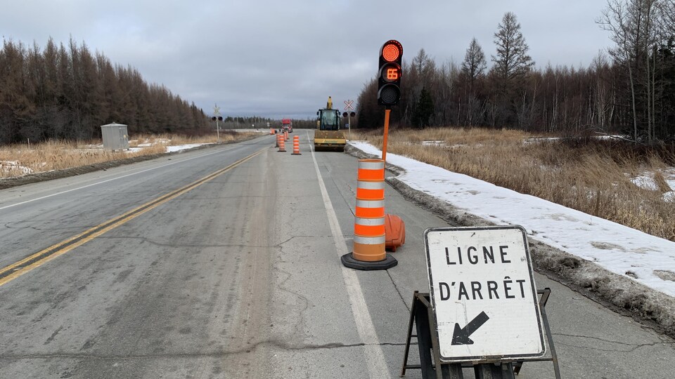 La ligne d'arrêt montre aux automobilistes où s'immobiliser sur la route. Le compteur indique 65 secondes avant de pouvoir repartir. Une pelle est immobilisée dans la zone de travaux.