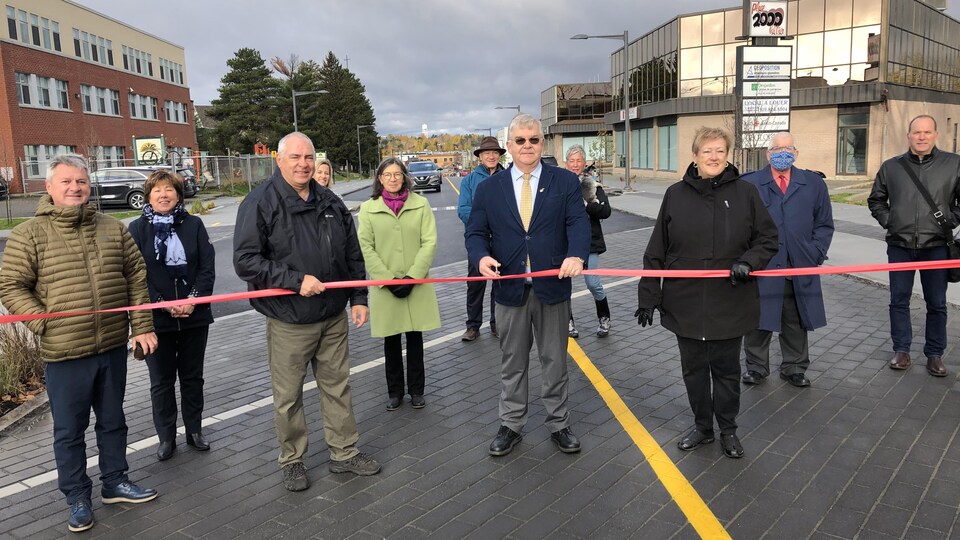 Une dizaine de personnes sont debout au milieu de la 3e avenue à Val-d'Or. Le maire s'apprête à couper le cordon rouge pour l'inauguration.