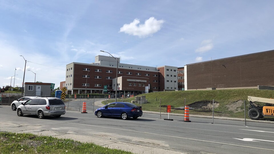 Des véhicules circulent près d'un chantier où on voit des cônes.