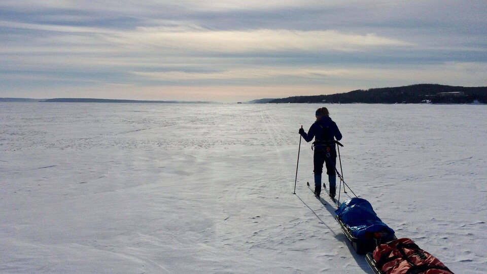 Sur un lac enneigé, une femme en ski de fond tire derrière elle deux traîneaux,