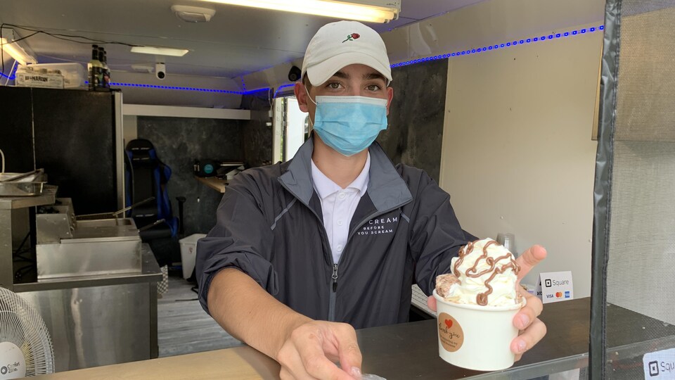 Un jeune homme tend une crème glacée et une cuillère au-dessus d'un comptoir.