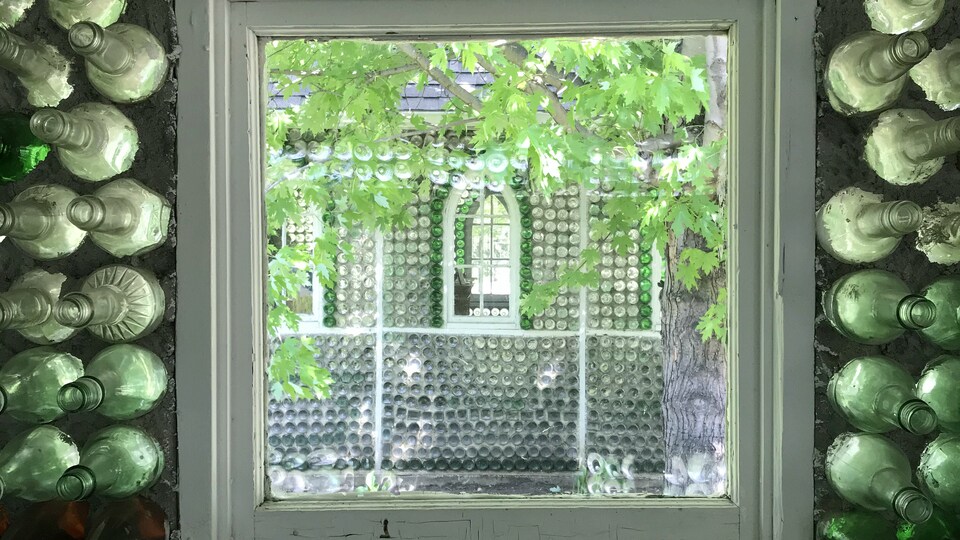 La fenêtre d'un batiment fait de bouteilles de verre permet de voir en partie le bâtiment d'à côté en verre lui aussi.