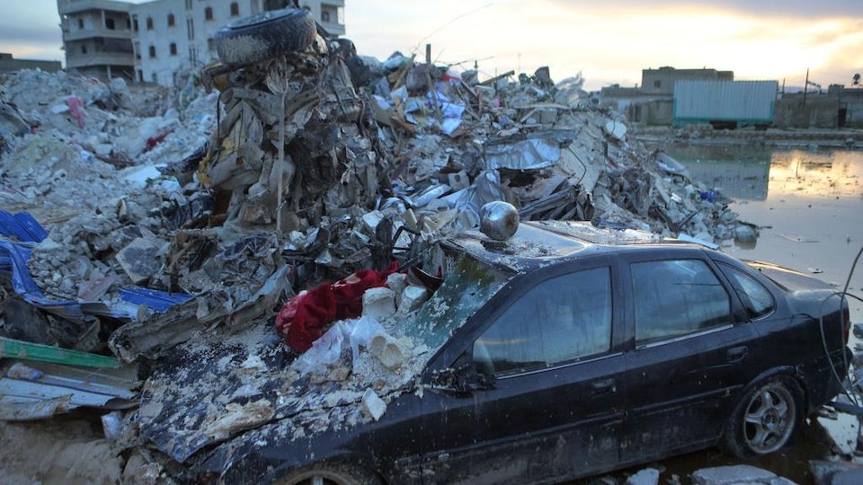 Une voiture est partiellement ensevelie sous les décombres d'un édifice à la suite d'un tremblement de terre en Syrie.
