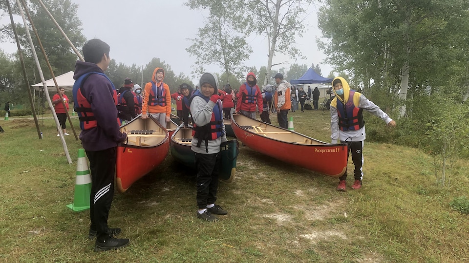 Des jeunes qui portent des gilets de sauvetage transportent des canots vers l'eau.