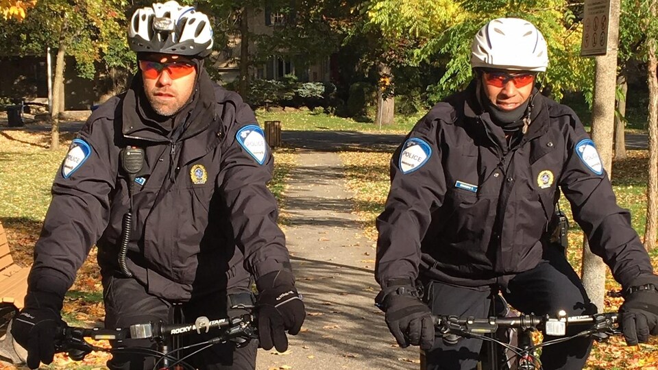 Les agents Olivier Archambault et Sylvain Brousseau patrouillent à vélo dans un paysage d'automne.