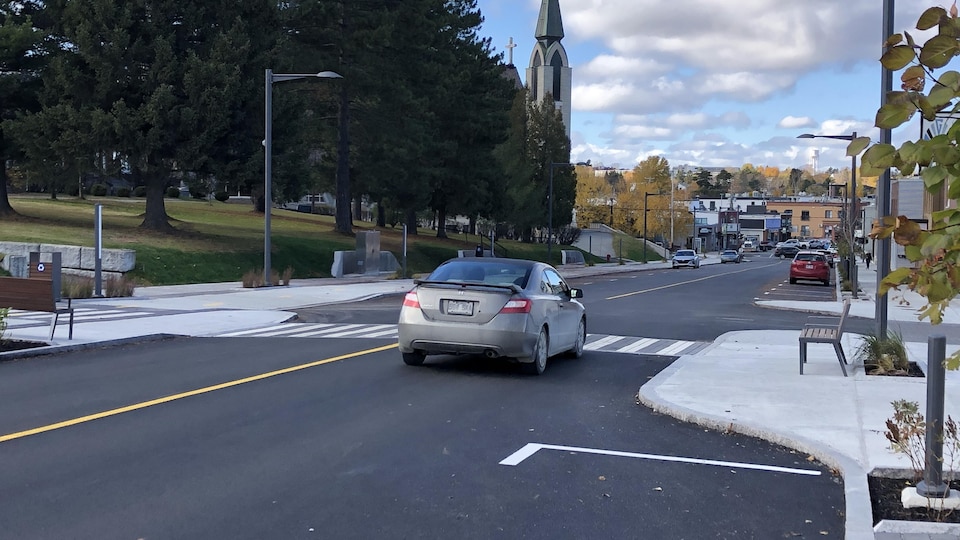 Une voiture circule sur une rue nouvellement revampée. Les gens peuvent circuler sur un passage pour piétons afin de traverser la rue.
