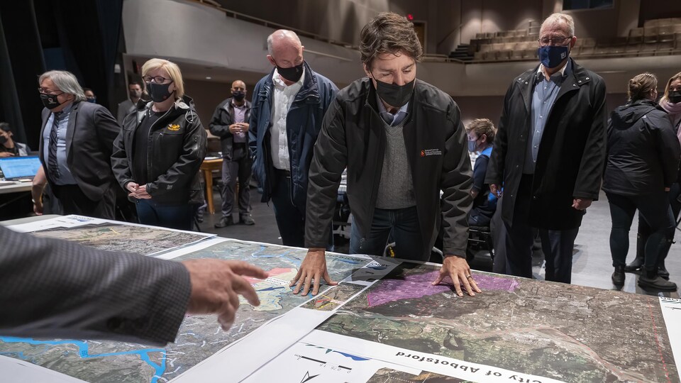 Justin Trudeau est penché vers l'avant et examine de grandes cartes géographiques déposées sur une grande table.