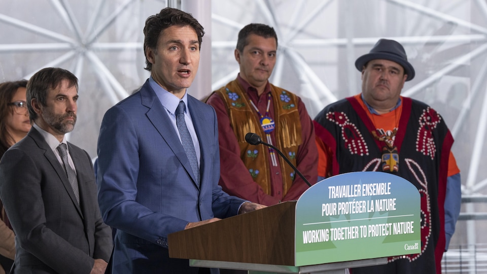 M. Trudeau, entouré des personnes mentionnées, prononce un discours devant un lutrin.