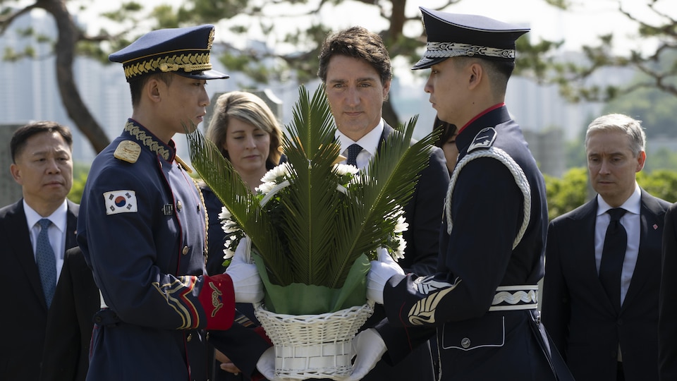 Un hombre y dos soldados sosteniendo una ofrenda floral.
