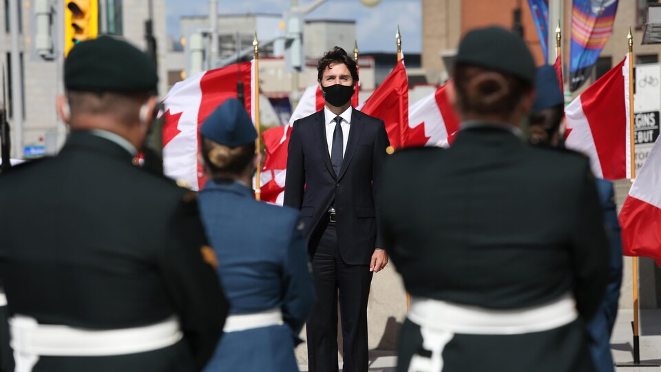 El Sr. Trudeau, enmascarado, parado frente a la hoja de arce, se enfrenta a soldados. 