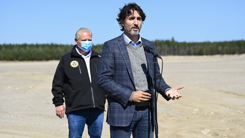 Justin Trudeau parle au micro, Doug Ford est derrière lui.