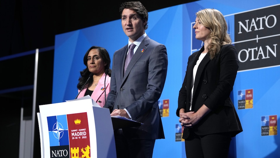 Justin Trudeau, entouré d'Anita Anand et de Mélanie Joly, sur un podium. 