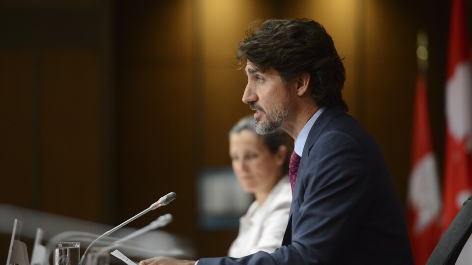 Plan moyen de Justin Trudeau de côté. En arrière-plan, Chrystia Freeland.