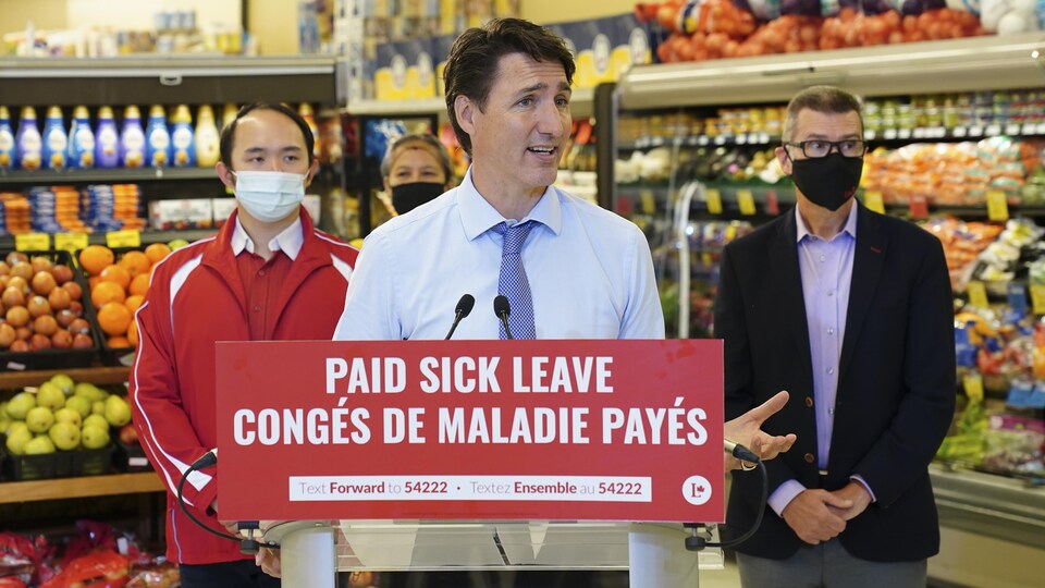 Justin Trudeau derrière un micro, entouré de candidats, dans une épicerie.