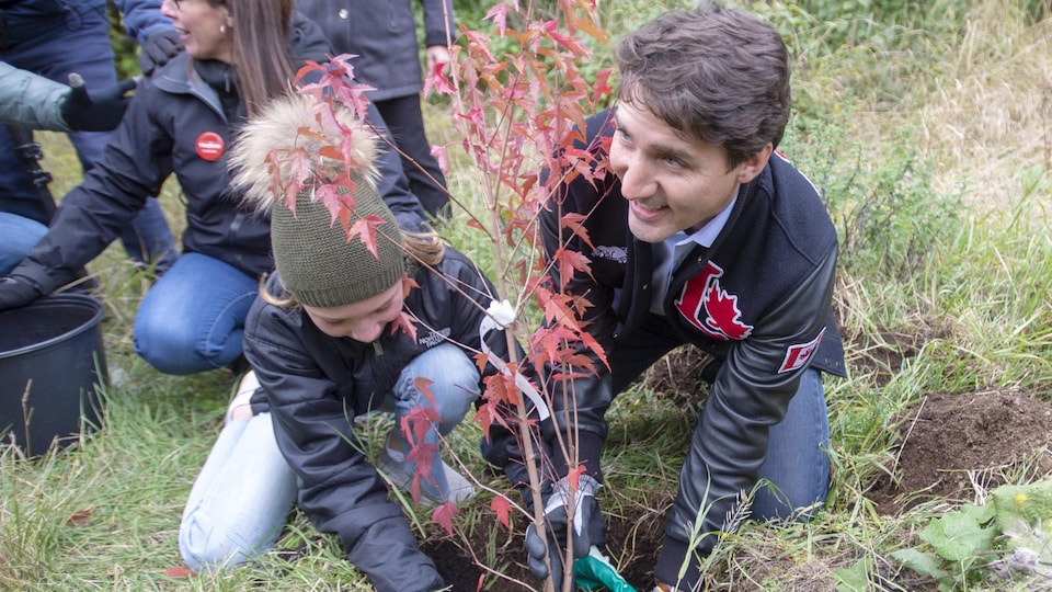 Justin Trudeau et sa fille, accroupis, plantent un arbre. 