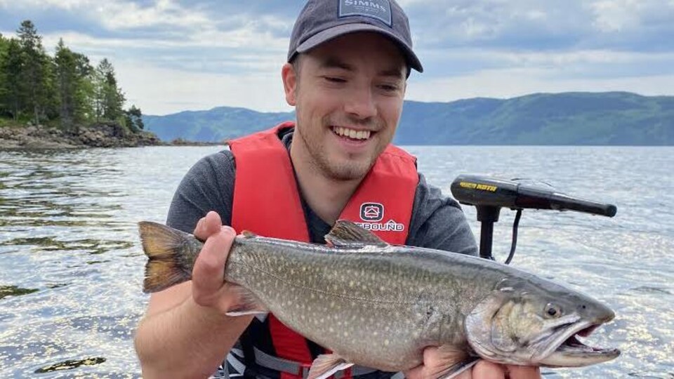 Un pêcheur heureux tient une truite dans ses mains.