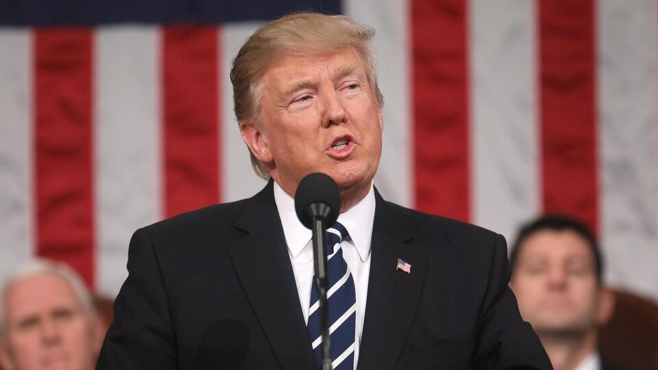 Le président américain Donald Trump derrière un micro et devant la drapeau américain, prononce son premier discours devant les deux chambres du Congrès.