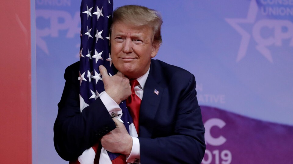 Le président américain Donald Trump serrant le drapeau américain dans ses bras avant de prononcer son discours au CPAC.