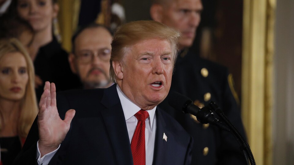Le président des États-Unis, Donald Trump, la main droite levée, lors d'une allocution à la Maison-Blanche concernant la stratégie de son administration dans la lutte aux opioïdes