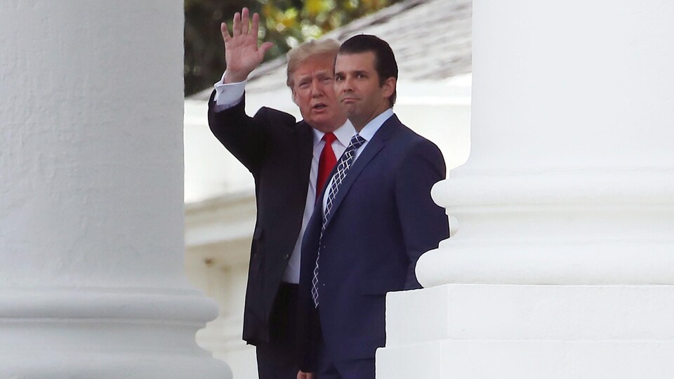 Le président Trump salue le photographe de la main alors que son fils regarde dans la même direction. Les deux hommes sont entre les colonnes blanches de la Maison-Blanche.