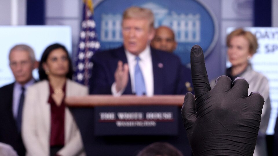 Un main gantée apparaît devant le podium de la tribune de la presse à la Maison-Blanche.