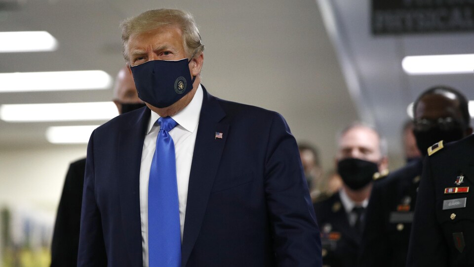 Donald Trump portant un masque bleu marine avec le blason doré de la présidence américaine gravé sur le côté gauche.