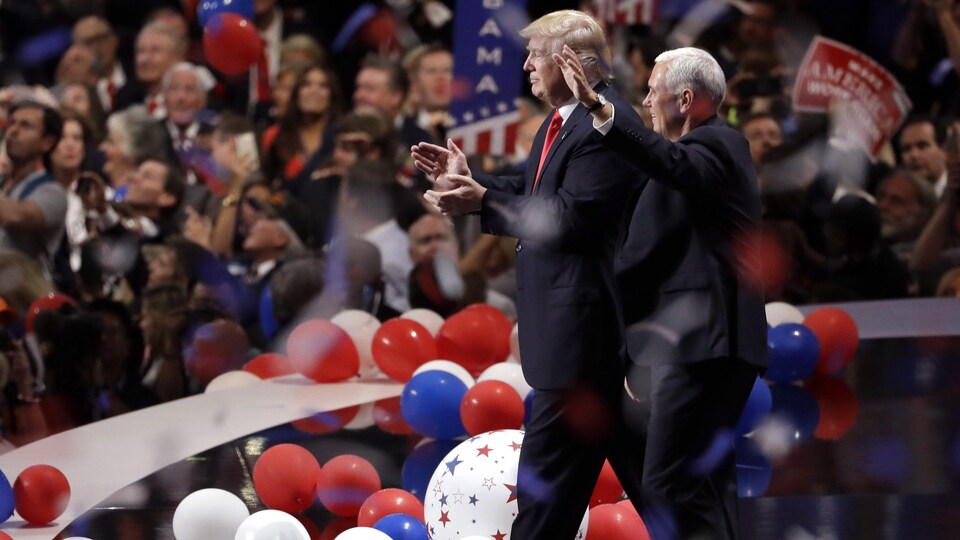 Donald Trump et Mike Pence marchant ensemble sur une scène jonchée de ballons, devant les partisans républicains, qui sont debout.