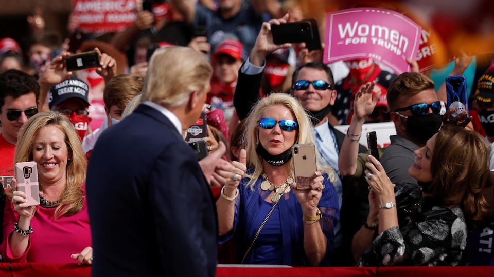 Donald Trump de dos devant des partisans. Il fait un signe de pouce en l'air à une femme, qui fait la même chose.