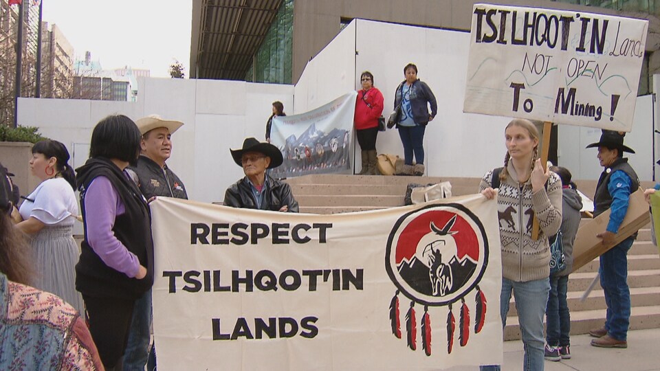 Des gens portent des pancartes qui disent "Respectez les terres Tsilqotin" et "Les terres Tsilquot'in ne sont pas ouvertes aux minières".