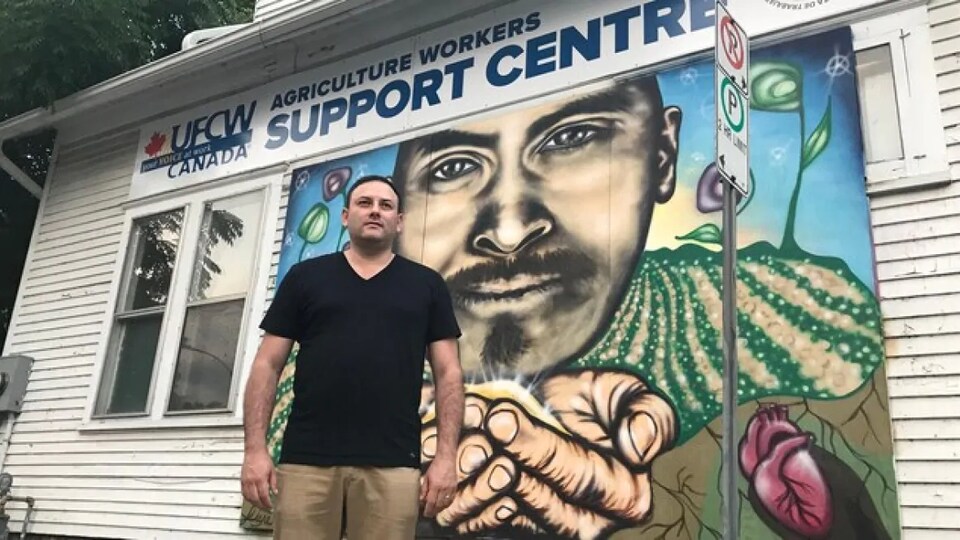 Un homme devant la façade d'un bureau ornée d'une murale. 