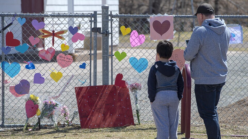 Un homme et un petit garçon sont debout, de dos, devant une clôture sur laquelle sont attachés des coeurs en papier et des messages.
