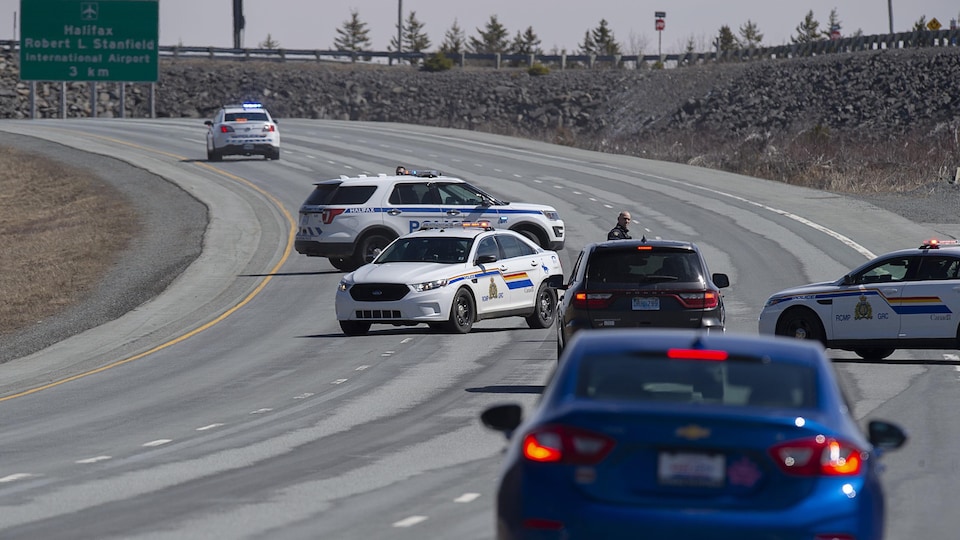 Trois voitures de police en travers d'une autoroute bloquent le chemin aux véhicules qui s'approchent.