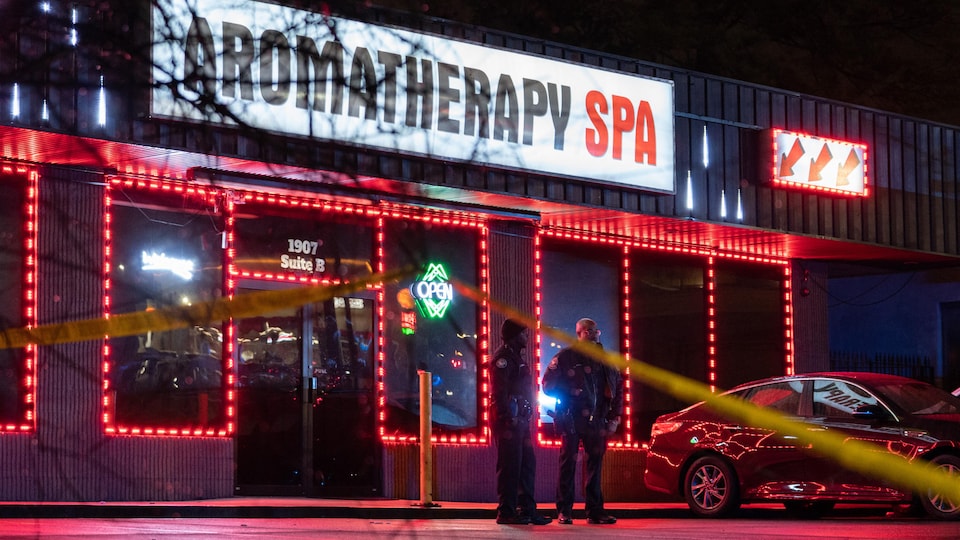 Des policiers devant un salon de massage éclairé par des néons.