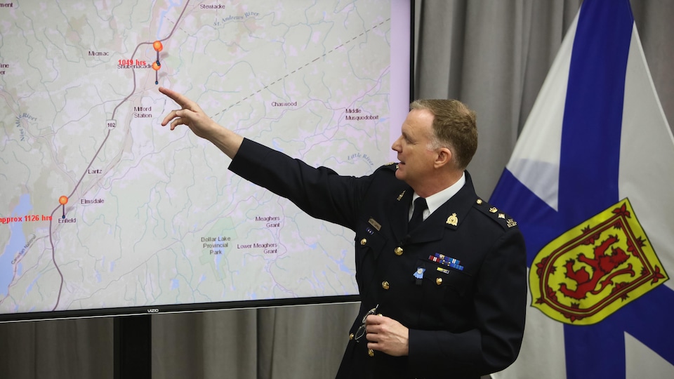 Un homme en uniforme de policier pointe un écran sur lequel on voit une carte routière et des indications indiquant une trajectoire.