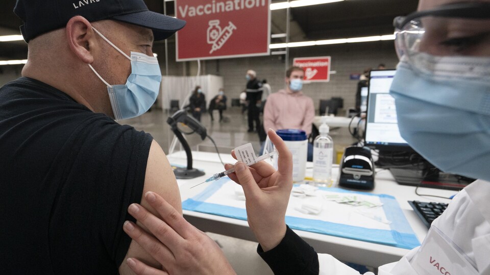 Un homme se fait vacciner par une préposée.