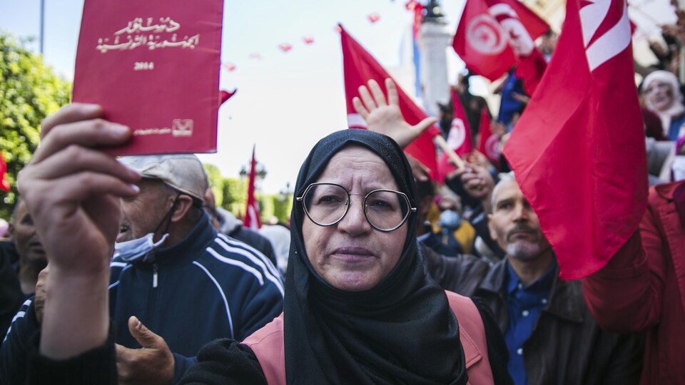 Debout au milieu d'une foule, une femme brandit une copie de la constitution de la Tunisie dans une manifestation tenue à l'extérieur.