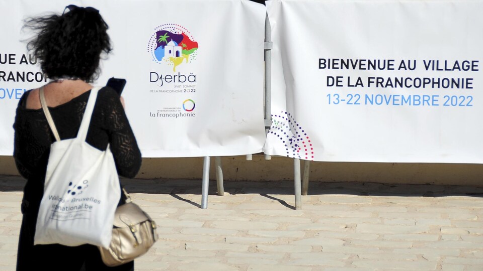 Un participant se tient devant des banderoles annonçant le 18e Sommet de la Francophonie à Djerba, en Tunisie.