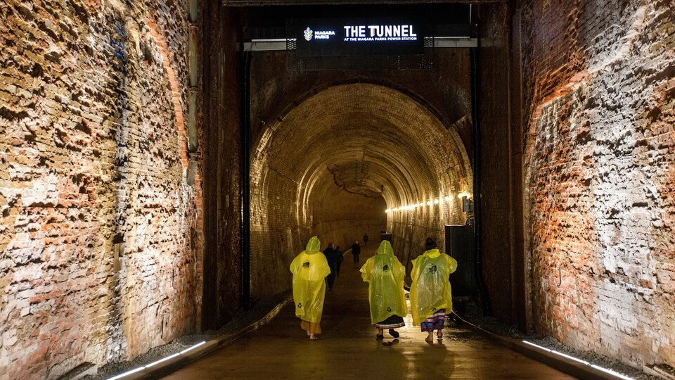 Des gens portant un imperméable marchent dans un tunnel.