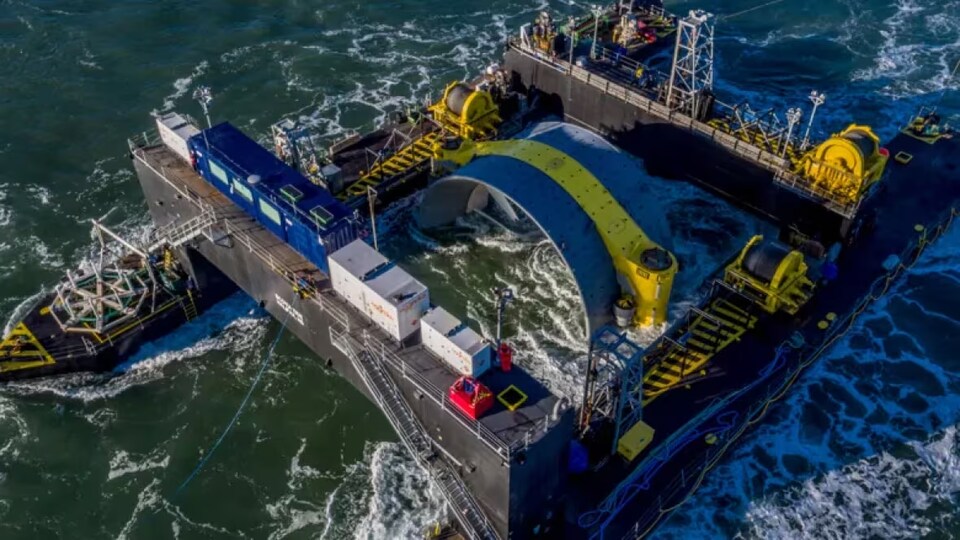 Une barge transporte une grosse turbine jaune et bleu.