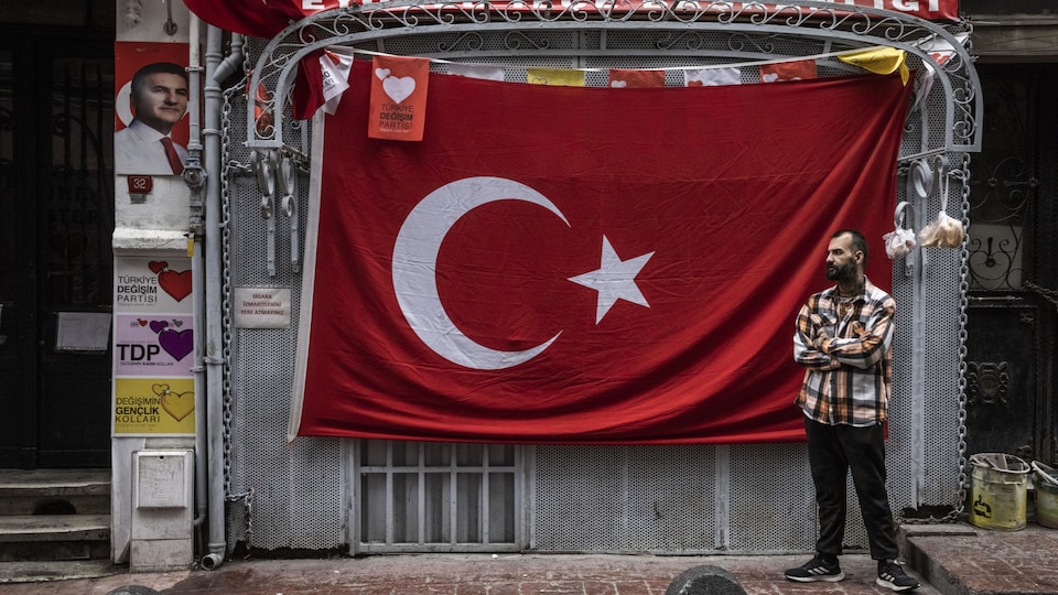 A man stands in front of a Turkish flag.