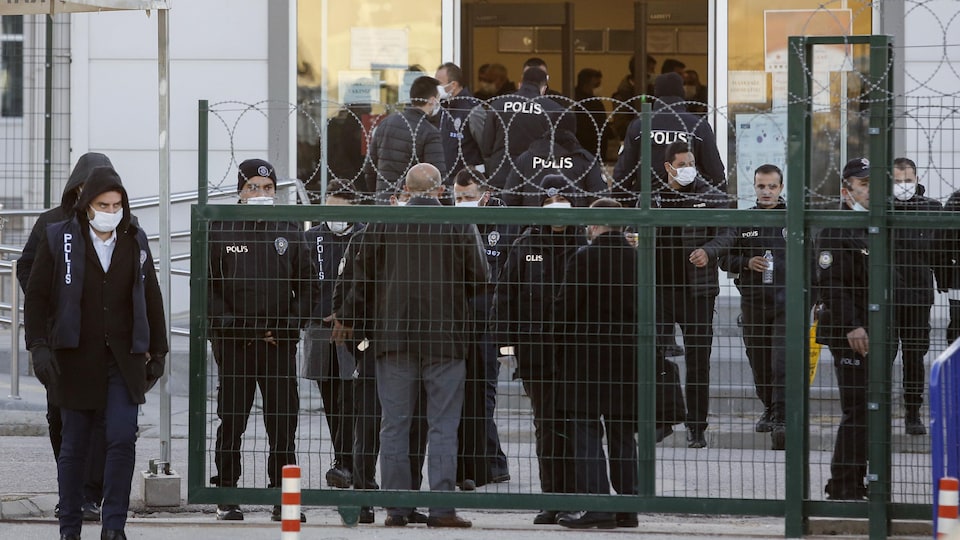 Plus d'une dizaine de policiers se trouvent derrière une clôture barbelée.