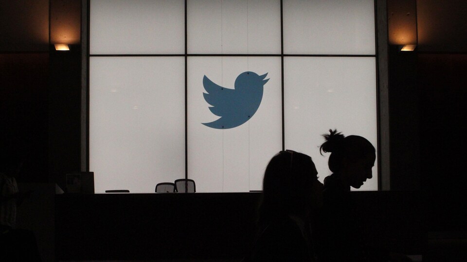 Un logo de Twitter dans un bureau ombragé. On voit également la silhouette d'une employée.